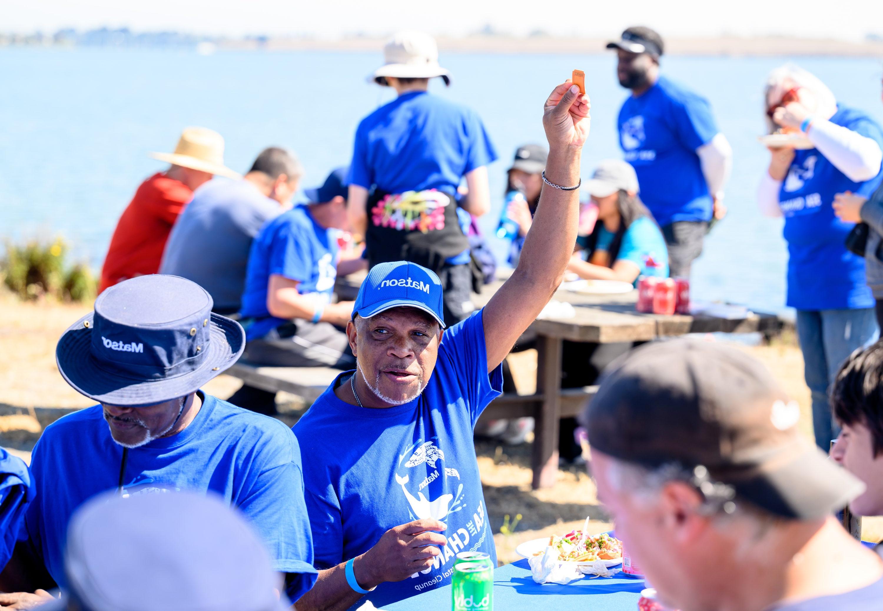 Volunteers sit and eat at picnic tables, while one volunteer holds his winning raffle ticket up in the air.